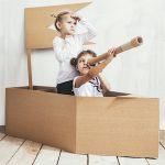 Two children little girls home in a cardboard ship play captains and sailors