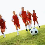 Team of athletic school children playing football in stadium