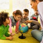 Group of preschoolers examining world globe with their teacher.